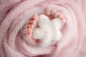 Knitted white star in the legs of a baby. Soft feet of a new born in a pink.