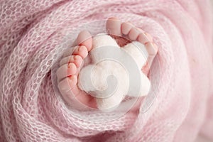 Knitted white star in the legs of a baby Soft feet of a new born in pink blanket