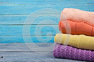 Knitted wool sweaters. Pile of knitted summer clothes on wooden background, sweaters, knitwear, space for text