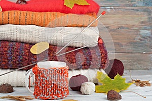 Knitted wool sweaters. Pile of knitted winter, autumn clothes on red, wooden background, sweaters, knitwear, ball, cup