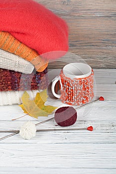 Knitted wool sweaters. Pile of knitted winter, autumn clothes on red, wooden background, sweaters, knitwear, ball, cup