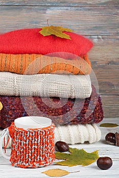 Knitted wool sweaters. Pile of knitted winter, autumn clothes on red, wooden background, sweaters, knitwear, ball, cup