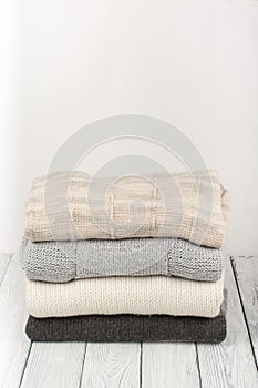 Knitted wool sweaters. Pile of knitted winter clothes on wooden background, sweaters, knitwear, space for text.