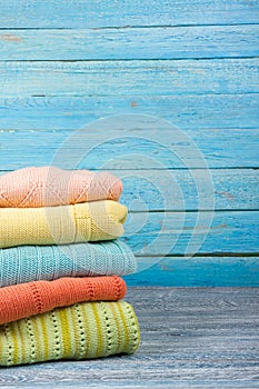 Knitted wool sweaters. Pile of knitted summer clothes on wooden background, sweaters, knitwear, space for text.