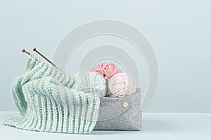 Knitting background. Knitting yarn, bamboo needles and new started knitted sweater in basket on light blue background