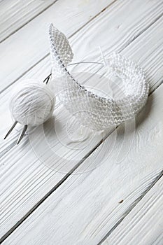 Knitting concept on white wooden background. Knitting needles and ball of white wool.