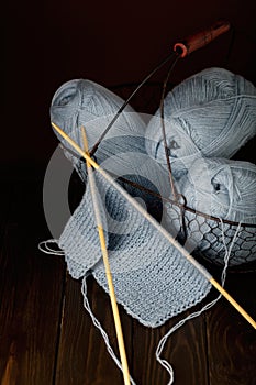 Knitting from light blue yarn on dark brown wooden background.