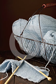 Knitting from light blue yarn on dark brown wooden background.
