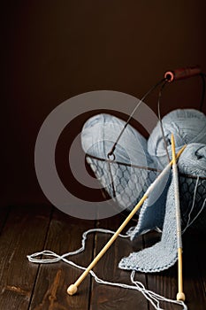 Knitting from light blue yarn on dark brown wooden background.