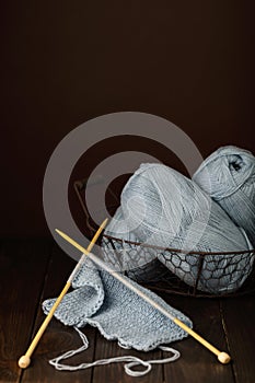 Knitting from light blue yarn on dark brown wooden background.