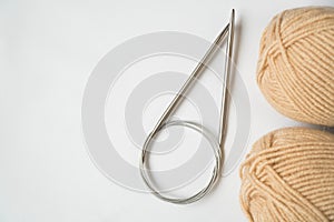 Knitting needles and two skeins of beige wool yarn on a white background. Copyspace. For for yarn stores, needlework, banner