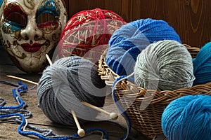 Knitting needles, wool balls and carnival mask on a wooden table