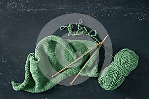 Knitting project with green wool and bamboo needles on rustic background