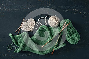 Knitting project with white and green wool and bamboo needles on rustic background