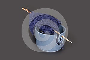 Knitting tools, ball of wool yarn for knitting and wooden needles. Blue yarns in a bowl isolated on dark gray background table.