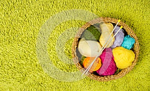 Knitting yarn balls, needles in basket over green carpet back