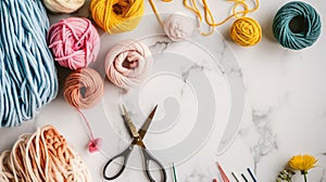 Knitting yarn balls in shades of pink, yellow, and blue, with scissors and hooks on a marble background