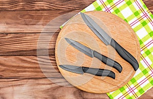 Knives with cutting board and kitchen towel on wooden table. Top view. Copy space