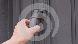 The knock of an old door knocker in the shape of a hand on a gray painted entrance