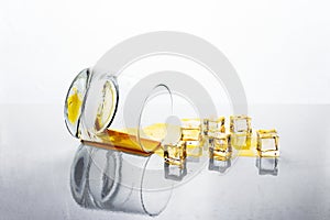 Knocked over glass of golden alcohol with ice cubes on white reflective surface, whiskey or cognac