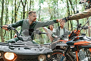 Knocking fists, gesture. Two couples on ATV with man that is on the bike in the forest