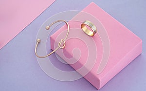 Knot shape golden bracelet and ring on pink and purple paper background with copy space