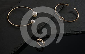 Knot shape and golden with pearls bracelets and chain shape ring on black stone surface