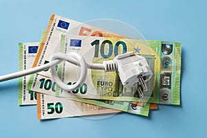 Knotted power cable with electric plug on 50 and 100 euro banknotes over blue background. Concept of rising energy costs in Europe