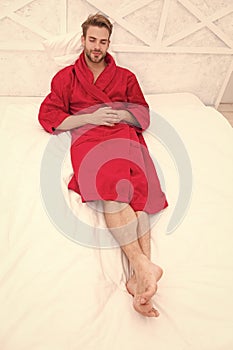 Knowing how to relax. Handsome man lying in bed to relax after bath. Sleepy guy in red bathrobe taking time to relax in