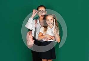 Knowledge day, Smiling funny little schoolkids sisters girls with backpack hold books on green blackboard. Childhood