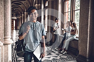 Knowledge empowers you.Handsome young student standing at the hall of campus and smiling