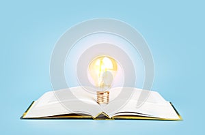 Knowledge study learning concept. Open book with a glowing light bulb on a blue background. Research, reading and study