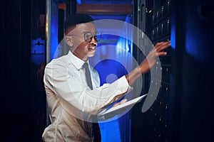 He knows his way around big data. a young man using a digital tablet while working in a server room.