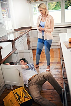 He knows a thing or two about plumbing. a man fixing pipes under his kitchen sink while his wife watches.