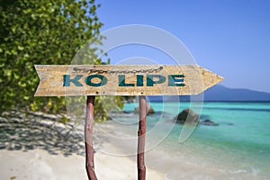 Ko Lipe wooden arrow road sign against tropical beach with white sand and turquoise water background. Travel and relaxation