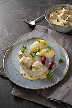 Koenigsberger Klopse or boiled meatballs in a white bechamel sauce with capers, potatoes and beetroot on a blue plate, dark gray photo