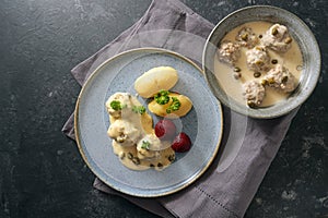 Koenigsberger Klopse or meatballs in white bechamel sauce with capers, potatoes and beetroot served in a bowl and on a gray blue photo