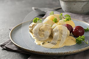 Koenigsberger Klopse or meatballs in a white bechamel sauce with capers, potatoes and beetroot served on a gray blue plate, photo