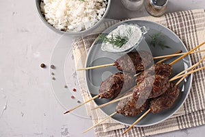 Kofta kebab on wooden skewers on a plate with sauce and a side dish of rice on the table, traditional dish of Arab cuisine,