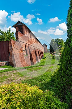 Kolomna kremlin red brick wall along green grass and foliage. Brickwork wall of the Kolomna Kremlin against blue cloudy sky