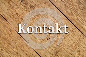 `Kontakt` white text on a wooden background. Translation: Contact