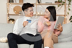 Korean Couple Shopping Online Using Digital Tablet Sitting At Home