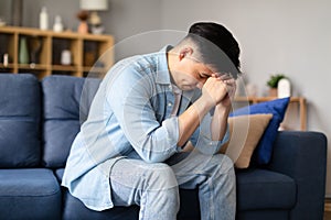 Korean guy crying resting head on fists sitting at home