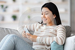 Korean Lady Messaging With Friends Or Browsing Internet On Smartphone At Home