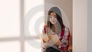 Korean Millennial Woman Reading A Book Sitting At Home