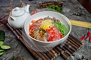 Korean noodle with kimchi, tomatoes, chili in white bowl on bamboo tray with tea pot