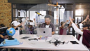 Korean schoolteacher with group of caucasian schoolchildren having lesson virtual reality using laptop and glasses VR