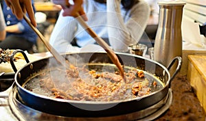 Korean spicy Kimchi bbq pork served on a hot pan with side dishes and rice as a background.