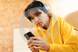 Korean Teen Boy Using Cellphone Wearing Wireless Headphones Sitting Indoors