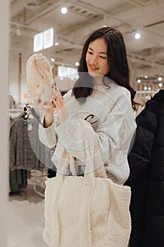 Korean teenage girl choosing and buying trendy clothes in a shopping mall. Retail and consumerism. Sale promotion and shopping